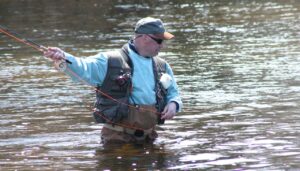 An angler in waders fly fishing in the Rhymney River, skillfully casting the line in search of trout.