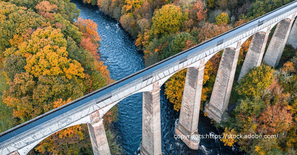 Aerial view of the Pontcysyllte Aqueduct with its iron walkway and towering stone pillars crossing over a river surrounded by autumnal trees.