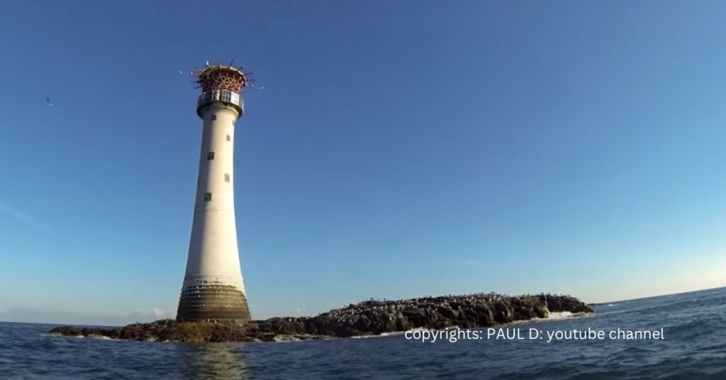 The Smalls Lighthouse standing tall on a rocky outcrop in the sea, with a clear blue sky in the background.
