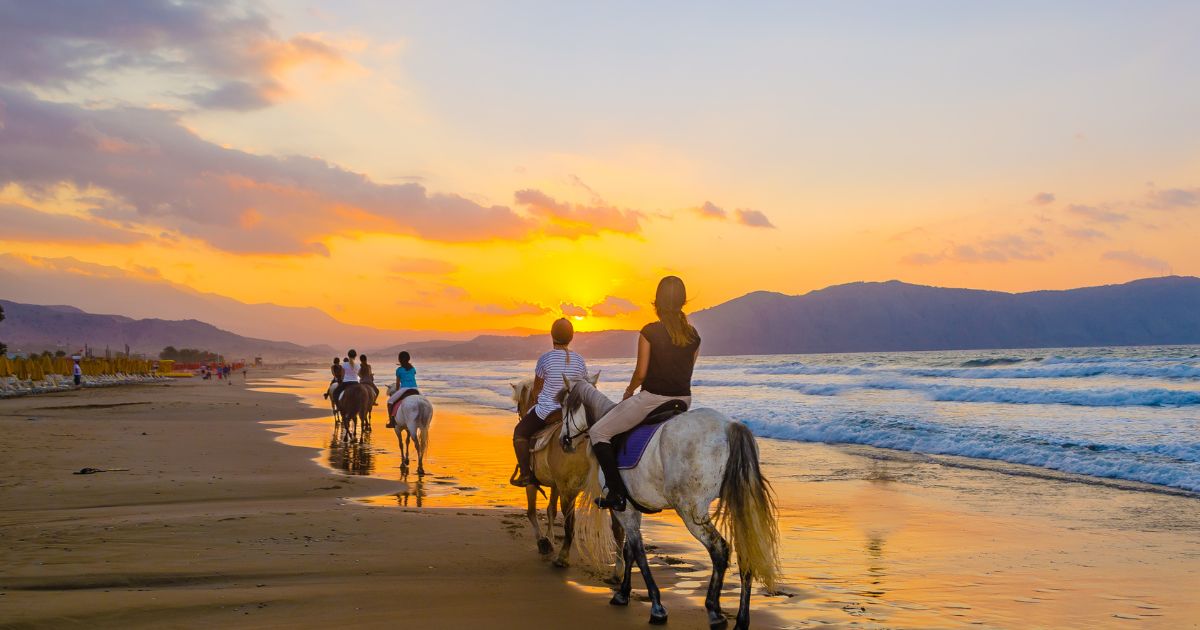 Horseback riders on an Anglesey beach at sunset, with vibrant skies and gentle waves, highlighting the island's natural beauty and recreational offerings.