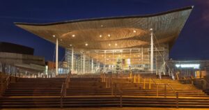 The Senedd Cymru building in Cardiff Bay at night, illuminated and showcasing modern architectural design, representing the political heart of Wales.