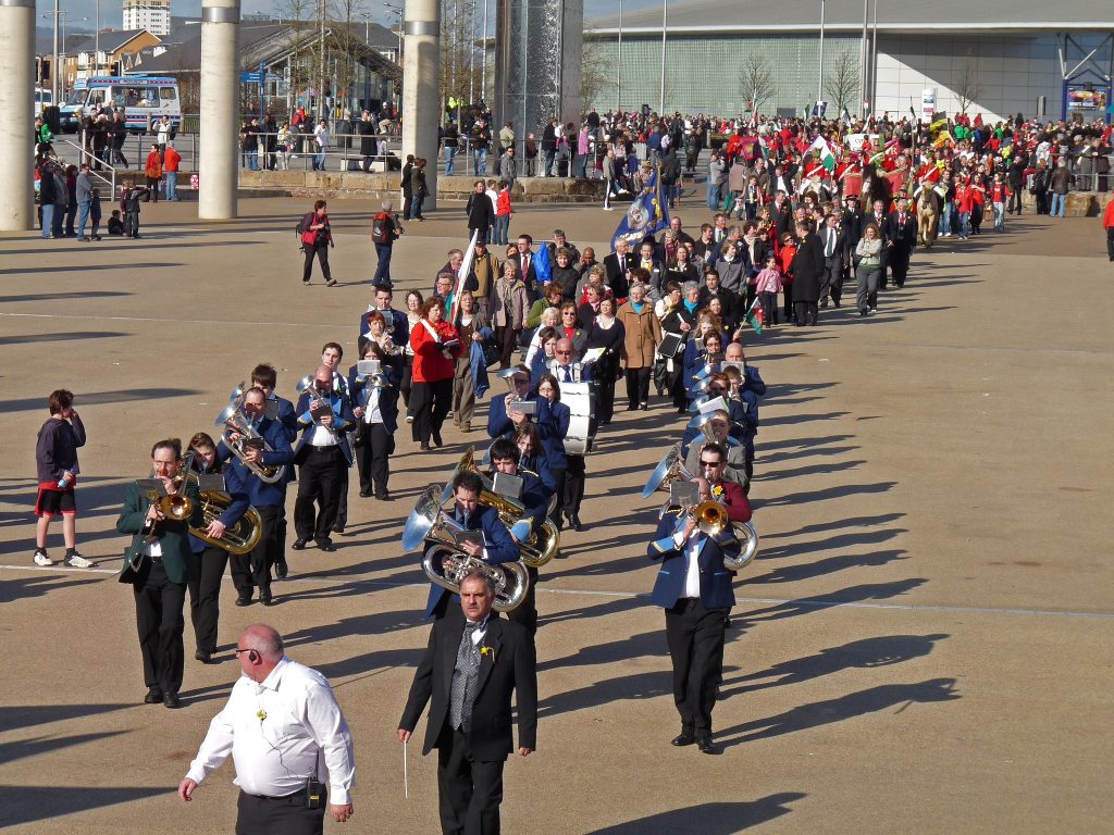 A marching band leads a St David’s Day parade with crowds following behind