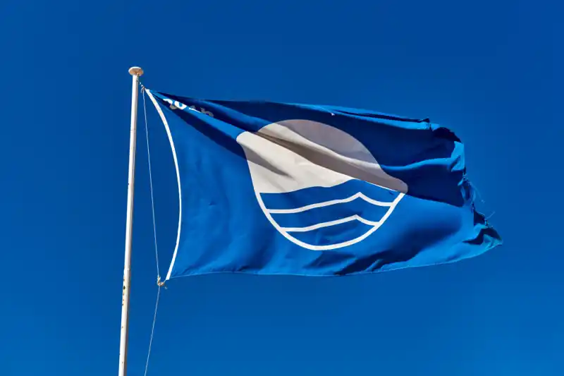 The Blue Flag award flying against a clear blue sky, symbolizing beach quality and environmental standards.