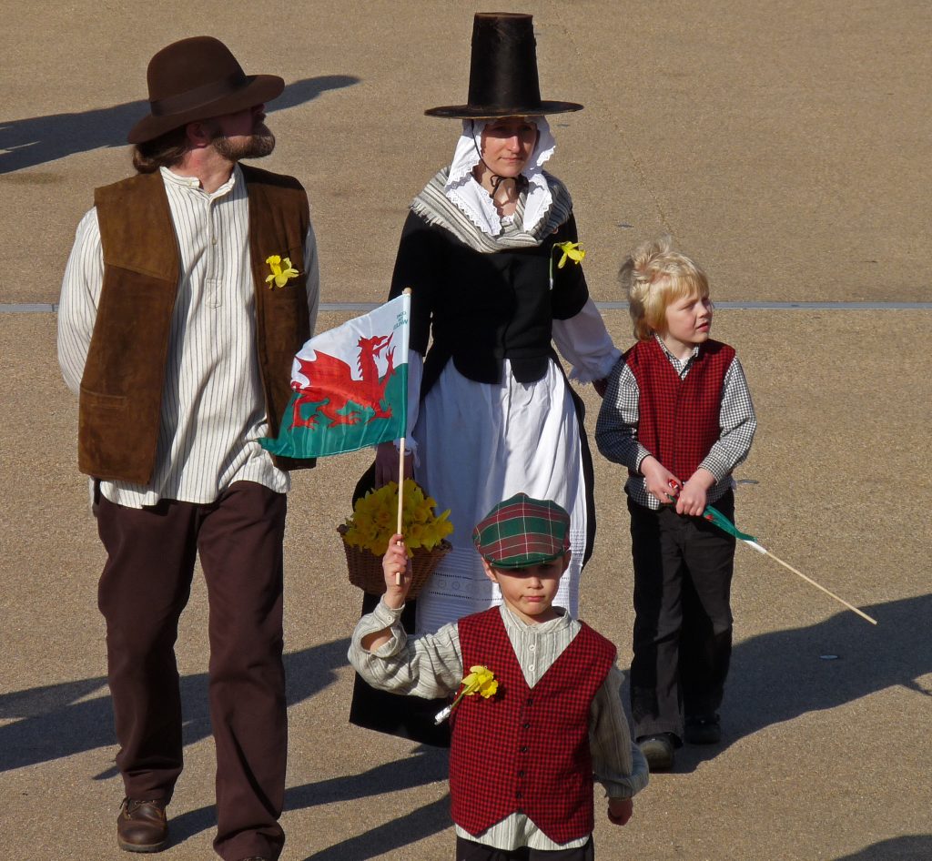 Children and adults in traditional Welsh costume holding a flag during a St David’s Day celebration