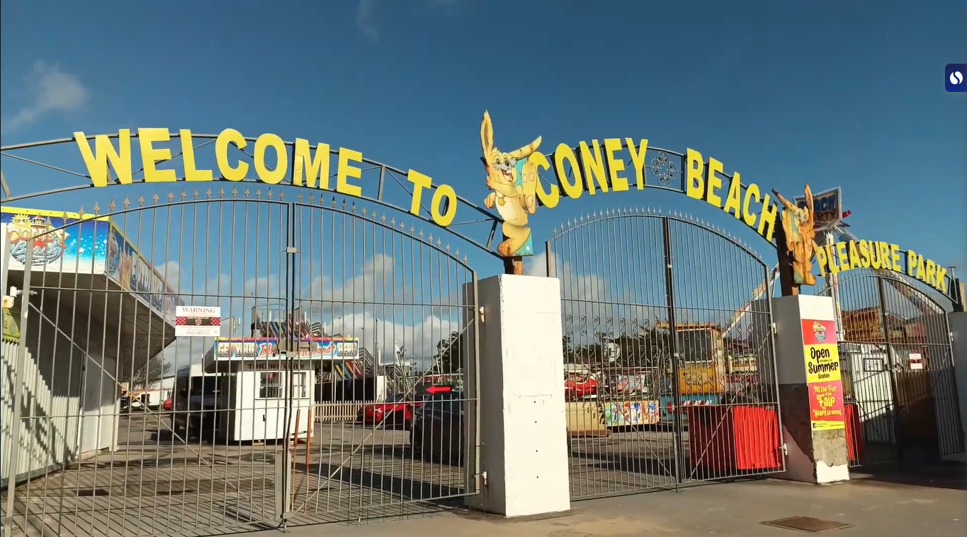 Entrance gate of Coney Beach Pleasure Park in Porthcawl, South Wales, with bright signage and blue skies.