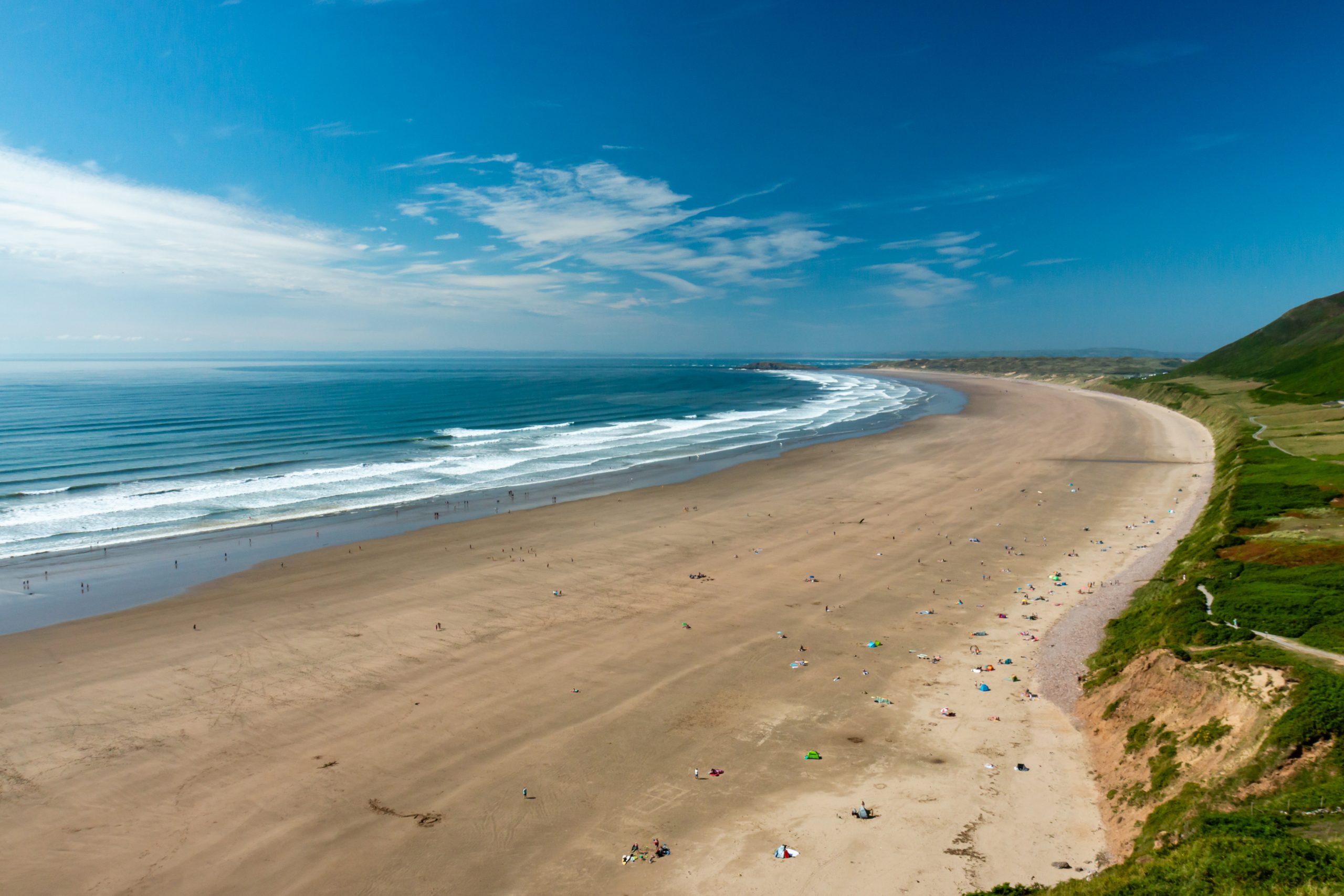 Wide view of Rhossili Bay’s three-mile sandy beach with gentle surf and coastal cliffs