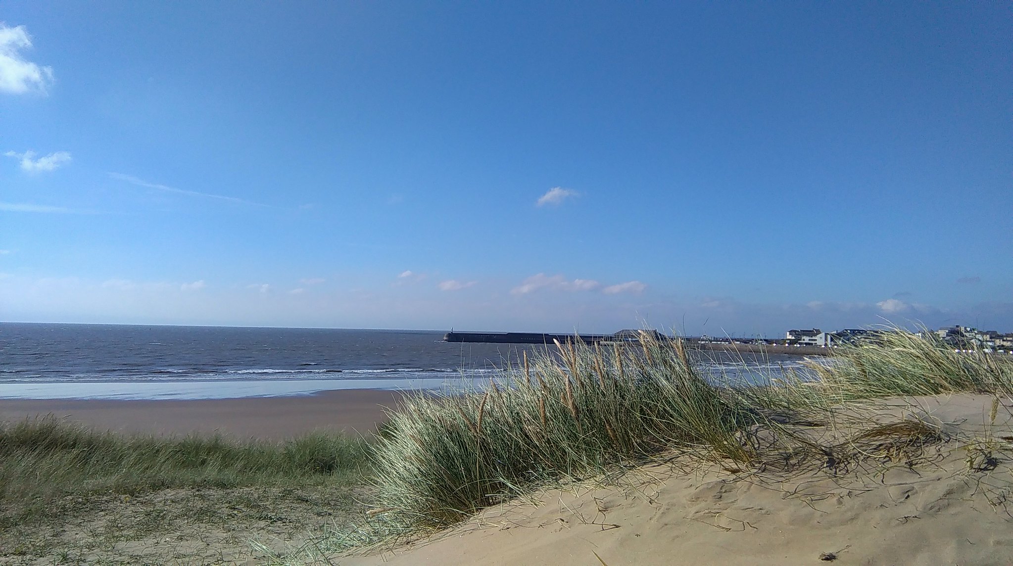 View of Sandy Bay (Coney Beach) in Porthcawl, South Wales, with sand dunes in the foreground and the sea and breakwater in the distance.
