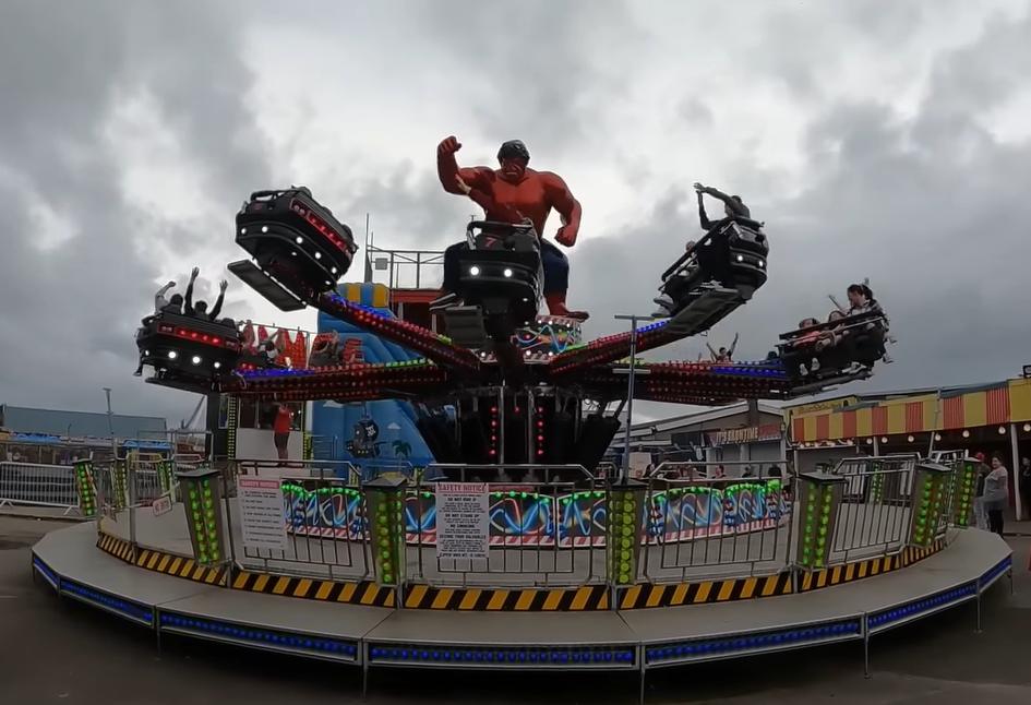 Visitors enjoying a spinning amusement ride at Coney Beach Pleasure Park in Porthcawl, South Wales, with a superhero figure in the center.