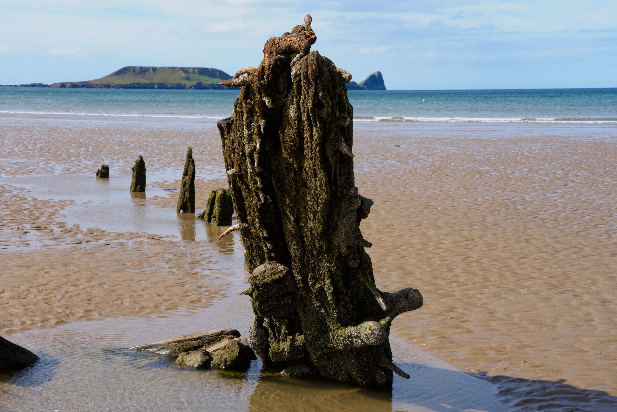 Remains of the Helvetia shipwreck on the sands of Rhossili Bay with Worm’s Head in the background