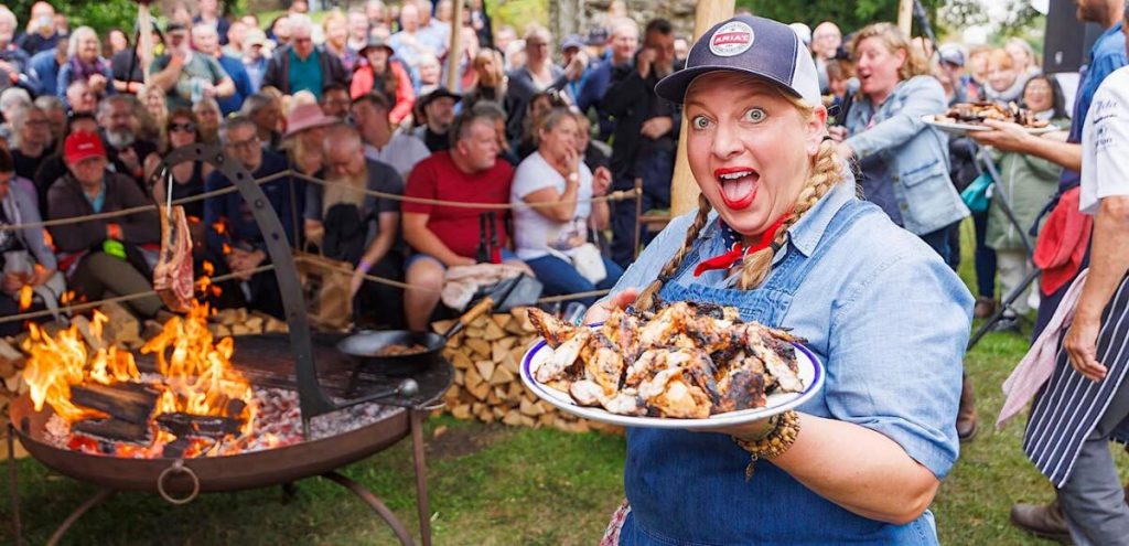 Cook presenting grilled food at Abergavenny Food Festival in South Wales with crowd in background