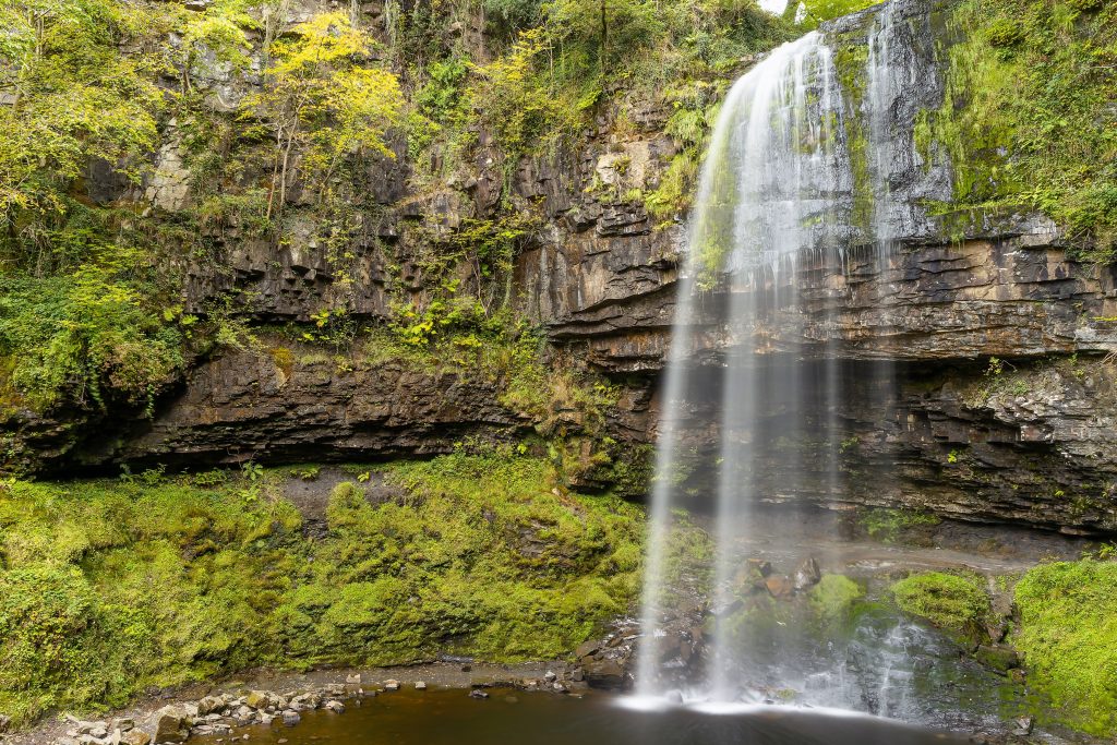 Henrhyd Falls surrounded by mossy cliffs and greenery in Brecon Beacons National Park