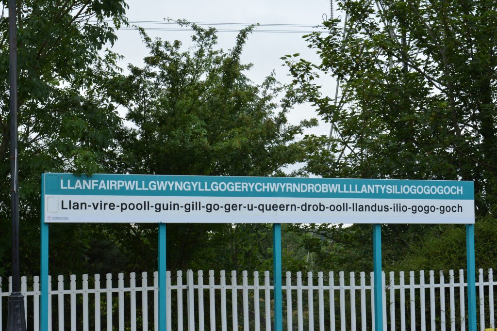 Sign displaying the full name of Llanfairpwllgwyngyllgogerychwyrndrobwllllantysiliogogogoch at the train station in Anglesey, Wales.