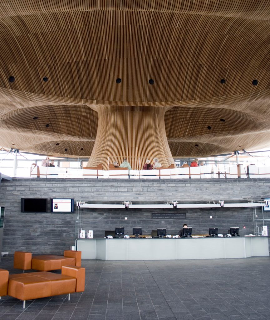 Interior view of the Senedd building in Cardiff, showcasing its unique wooden ceiling and public reception area.