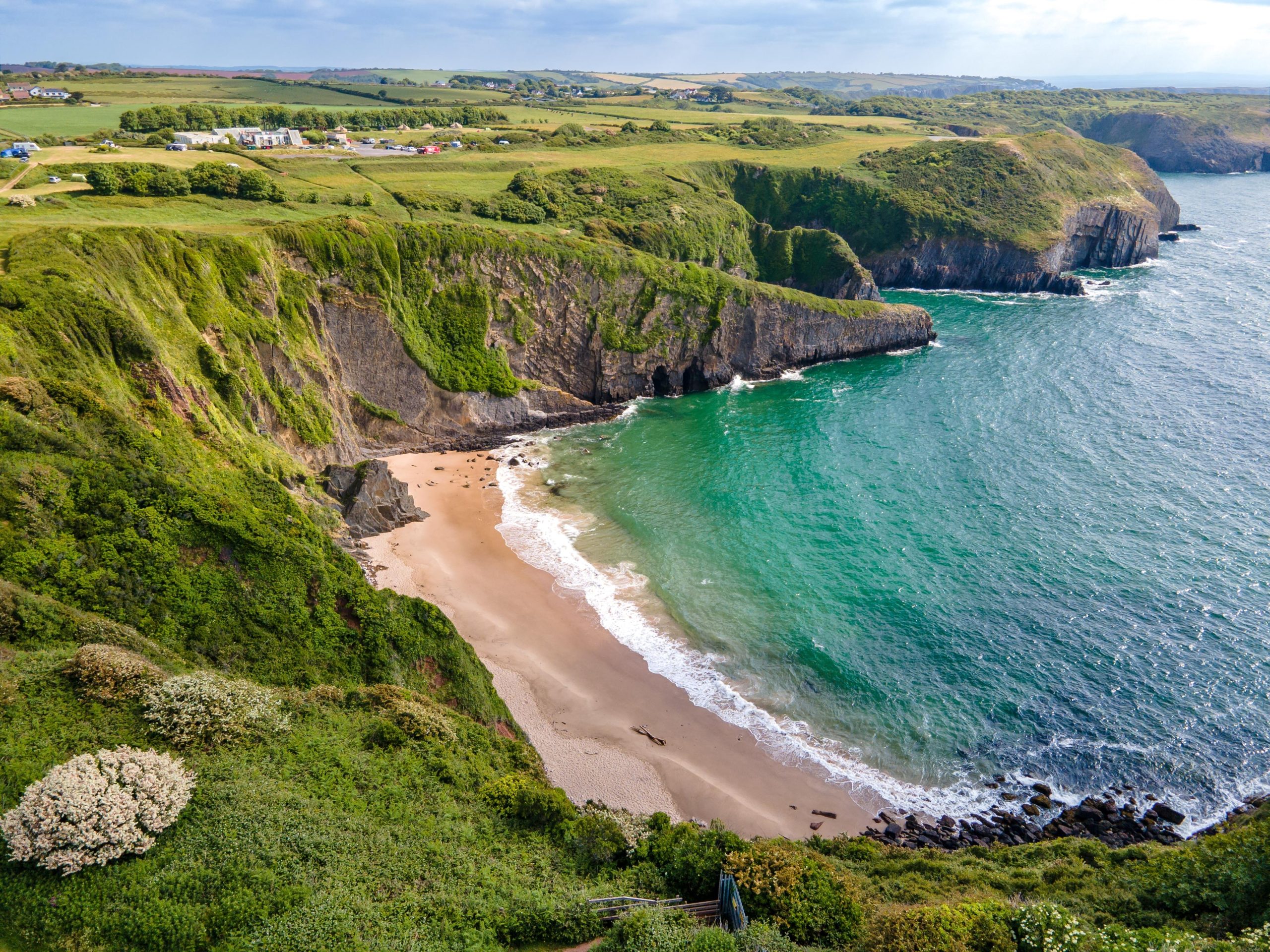 Aerial view of Shrinkle Haven and Church Doors Cove on the Pembrokeshire coast, Wales, showing sea cliffs, a sandy beach, and turquoise waters.